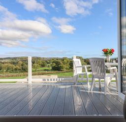 A patio with white chairs and a table with flowers overlooking a green landscape at Chestnut Lodge in Teigngrace near Newton Abbot