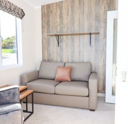 A small living room with a gray sofa and single orange pillow a gray armchair two nested wooden tables and a window at Chestnut Lodge in Teigngrace near Newton Abbot