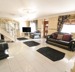 A living room with black leather sofas black rugs a television and ornate curtains at Bryn Berthen in Penrhyndeudraeth