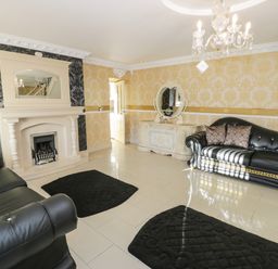 A living room with black leather sofas a fireplace mirror chandelier and rugs at Bryn Berthen in Penrhyndeudraeth