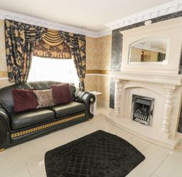 A living room with a black leather sofa with cushions a fireplace and patterned curtains at Bryn Berthen in Penrhyndeudraeth