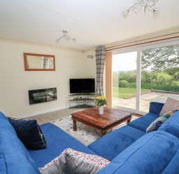 A living room with blue couches a wooden coffee table and a TV near a sliding glass door at Erwlon in Rhydyfelin near Aberystwyth