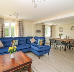 A living room with a blue sectional sofa and wooden coffee table with flowers at Erwlon in Rhydyfelin near Aberystwyth