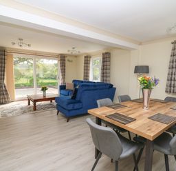 A living room with blue sofas a wooden dining table with chairs and flowers on it at Erwlon in Rhydyfelin near Aberystwyth
