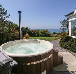 An outdoor hot tub with bubbling water near a house with garden and sea view at Fron Olau in Nefyn