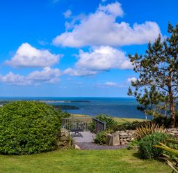 A garden with bushes trees and a bench overlooking the sea at Fron Olau in Nefyn