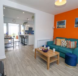 A living room with teal sofa and wooden coffee table next to an open kitchen with bar stools at Lagoon View in Wyke