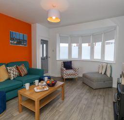A living room with a teal sofa and wooden coffee table with snacks and drinks a patterned armchair and grey chaise lounge by bay windows at Lagoon View in Wyke