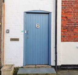 A blue door with number 6 on a white and red brick wall next to a window at Tuckaway Cottage in Aldeburgh