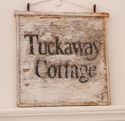 A weathered wooden sign with the words Tuckaway Cottage on a white wall at Tuckaway Cottage in Aldeburgh