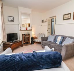A living room with a grey sofa blue cushions a TV on a wooden chest a fireplace and an armchair at Tuckaway Cottage in Aldeburgh