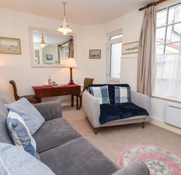 A living room with two sofas a desk with a lamp and chairs a large window and a round rug at Tuckaway Cottage in Aldeburgh