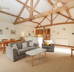 An open living room and kitchen with wooden beams on the ceiling a grey sofa and armchair a dining table and wooden cabinets at Peartree Cottage Stanford Bishop near Bromyard