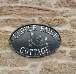 A stone wall with a black oval sign reading Clover Patch Cottage