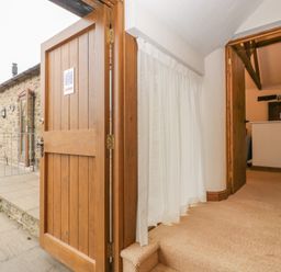 A hallway with an open wooden door leading outside to a stone patio and a stone building at Honeysuckle Cottage in Stanford Bishop near Bromyard