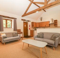 A living room area with two gray sofas and a coffee table in front of a kitchen with wooden cabinets and exposed wooden ceiling beams at Honeysuckle Cottage Stanford Bishop near Bromyard