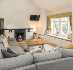 A living room with a grey sofa around a wooden coffee table a fireplace a wall-mounted TV and window seating at Lakeside Cottage in Llanrug