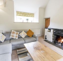 A living room with a grey sofa cushions wooden coffee table and a fireplace at Lakeside Cottage in Llanrug
