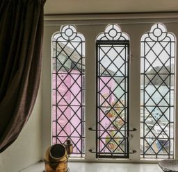 A window with lattice design overlooking pink buildings and a harbor at 1 The Old Brewhouse in Dartmouth