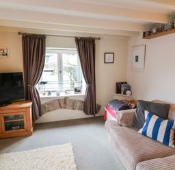 A living room with a sofa with striped cushions a television on a wooden cabinet and curtains on a window at 1 The Old Brewhouse in Dartmouth
