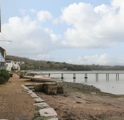 A waterfront path next to stone buildings with boats and a pier over water at 1 The Old Brewhouse in Dartmouth