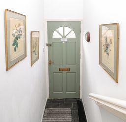 A hallway with a green door at the end with framed botanical prints on white walls and a striped rug on the floor at 60B Castlegate in Berwick-Upon-Tweed