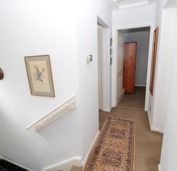 A hallway with a patterned runner rug a wall clock floral picture and a wooden wardrobe visible through an open door at 60B Castlegate in Berwick-Upon-Tweed
