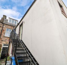 An exterior staircase leading to an upper door of a white building next to a stone building with windows at 60B Castlegate in Berwick-Upon-Tweed