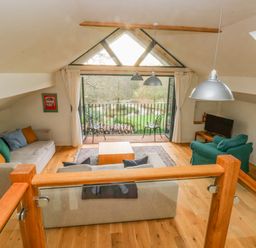 A living room with sofas a coffee table and a balcony overlooking a garden at Green Grove Barn in Peniel near Carmarthen