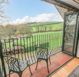 A balcony with two black chairs and metal railing overlooking green fields and trees at Green Grove Barn in Peniel near Carmarthen