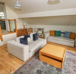 A living room with two sofas a wooden coffee table bookshelf and stairs at Green Grove Barn in Peniel near Carmarthen
