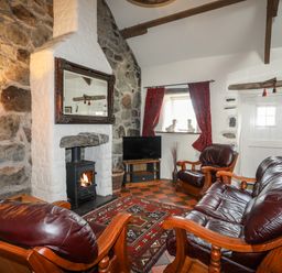 A living room with leather chairs a fireplace a TV and red curtains at Tir Eironwy in Dinas near Nefyn