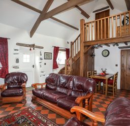 A living room with leather sofas a dining table wooden staircase and a loft at Tir Eironwy in Dinas near Nefyn