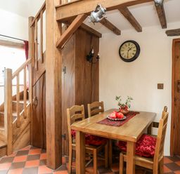 A dining area with wooden table and chairs by wooden stairs and a wall clock at Tir Eironwy in Dinas near Nefyn