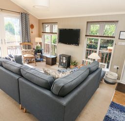 A living room with a gray sectional sofa a wooden chair a wall-mounted television and a door at 1 Hornbeam Lodge Narberth