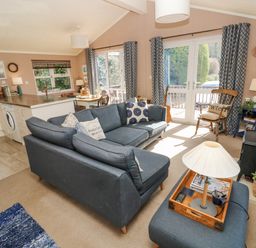 A living room with a blue sofa set a wooden chair a lamp and a kitchen area in the background at 1 Hornbeam Lodge in Narberth