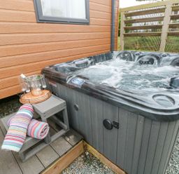 An outdoor hot tub with bubbling water next to a wooden wall with a small wooden step holding a tray with a bottle on ice and four glasses and two rolled towels at Seahorse Retreat in Little Haven near Broad Haven