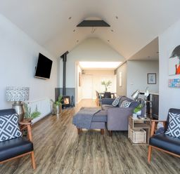 A living room with chairs pillows a sofa a TV and a dining table at Haulfryn in Moelfre