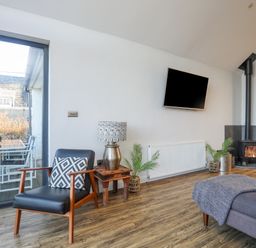 A living room with a black armchair wooden side table lamp wall mounted tv wood stove and glass door to patio at Haulfryn in Moelfre