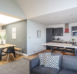 An open plan kitchen and dining area with a wooden dining table and chairs and a kitchen island with stools at Haulfryn in Moelfre
