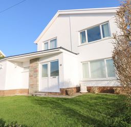 A house with white walls green lawn and leafless tree at 30 Long Shepherds Drive in Newton near The Mumbles