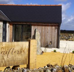 A farmhouse exterior with stone and wooden walls a wooden sign reading Menifters and a garden area at The Rum House in Porthallow