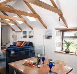 A kitchen and living area with wooden beams glass railing blue sofa and dining table at The Rum House in Porthallow