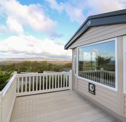 A deck with white railing outside a mobile home with windows showing countryside and hills at Gwent 74 in Borth