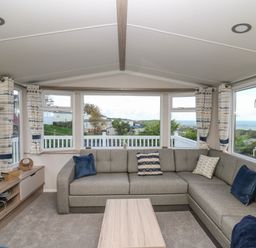 A living room with a gray sectional sofa blue and patterned cushions a wooden coffee table and a TV unit with a television at Gwent 74 in Borth