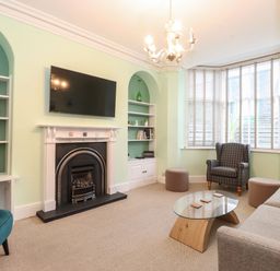 A living room with a fireplace a wall mounted tv a glass coffee table a sofa an armchair and bay window blinds at Blencathra in Keswick
