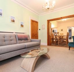 A living room with a gray sofa a glass coffee table and a blue armchair with a dining area visible through wooden sliding doors at Blencathra Keswick