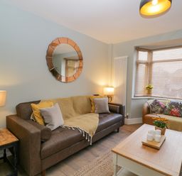A living room with two sofas a coffee table a round mirror on the wall and windows with blinds at Birch House in Corsham