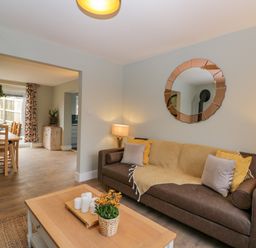 A living room with a brown sofa, cushions, a round mirror above, and a wooden coffee table with candles and flowers at Birch House in Corsham