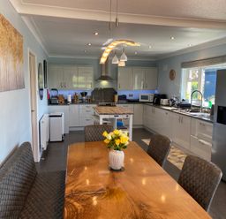 A kitchen with white cabinets a wooden dining table with chairs and a bench a vase with flowers a refrigerator and kitchen appliances at Ashlea in Launceston